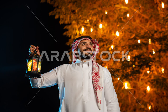A Saudi Gulf Arab man holding a Ramadan lantern, lighting and decorations for the month of Ramadan, Ramadan lantern, the blessed month of Ramadan, Ramadan atmosphere, religious occasions