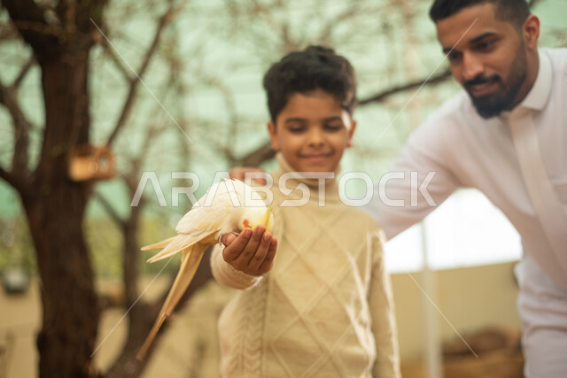 A Saudi Arabian Gulf man accompanied by his son, spending fun times in the zoo in the Kingdom of Saudi Arabia, recreational activities with birds, breeding and training birds in the nature reserve.
