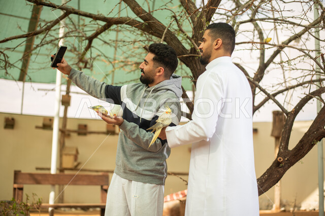 رجلان عربيان خليجيان سعوديان استخدام الهاتف المحمول ، التقاط صور تذكارية ، أنشطة ترفيهية مع الطيور ، محمية طبيعية ، فعالية سفاري موسم الرياض.