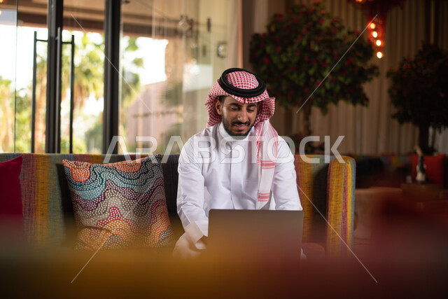 رجل عربي خليجي سعودي ينجز اعماله باستخدام الحاسوب المحمول ، العمل عن بعد ، انجاز مهام العمل ، تصفح الانترنت ، استخدام تقنيات حديثة.