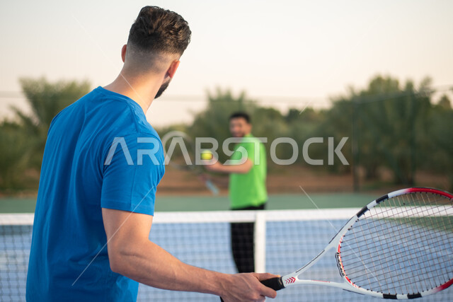 شابان عربيان خليجيان سعوديان يمارسان كرة التنس الأرضي، لعب كرة المضرب في الملاعب العامة، العاب رياضية، ملعب رياضي، تدريبات رياضية، مضرب رياضي، انشطه ترفيهيه رياضية، انشطة ورياضات شبابية، نشاط بدني