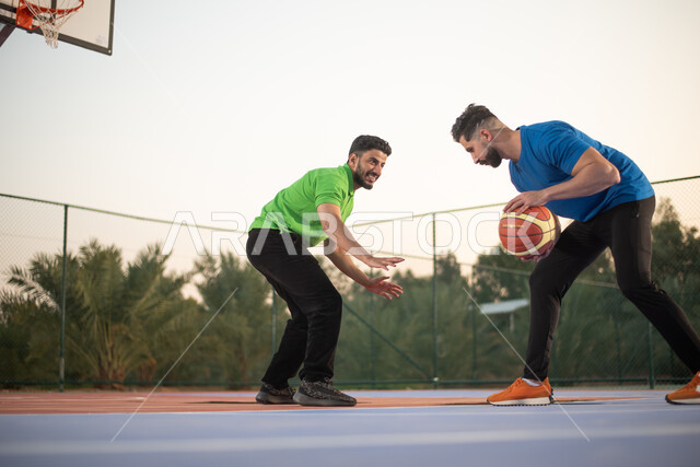 Two Saudi Arabian Gulf friends playing basketball, practicing basketball in public courts, sports entertainment activities, clubs and encouragement, youth activities and sports, competitions and challenges, physical activity