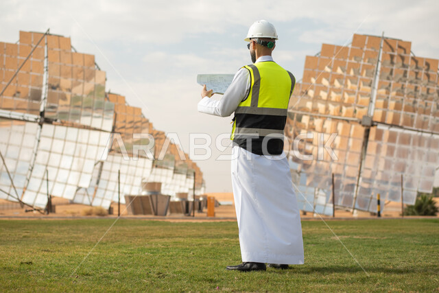 A Saudi Arabian Gulf energy engineer holding a map in his hand and supervising solar power plants in the Kingdom of Saudi Arabia, wearing a helmet and work protection jacket, Saudi Vision 2030, renewable energy, clean energy, natural energy, satellite, so