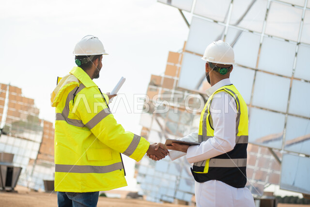 مهندسان طاقة عربيان خليجيان سعوديان يتصافحان، الاشراف على محطات الطاقة الشمسية في السعودية، مخططات وتصاميم هندسية، حوارات ونقاشات، إرتداء خوذة وسترة الحماية الخاصة بالعمل، الطاقة المتجددة، الطاقة النظيفة، الطاقة الطبيعية، ستلايت، محطات الطاقة الشمسية