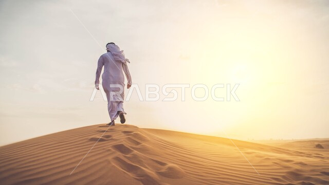 لقطة من الخلف لرجل خليجي يمشي في الصحراء، غروب الشمس في صحراء عين العتيق، أثر الخطوات على الرمل