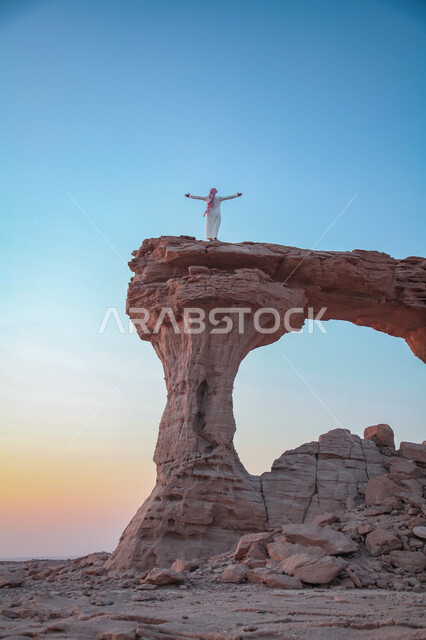 رجل عربي سعودي خليجي يقف على جبل صخري,القوس الصخري في خشم أبو مخروق ، جبال طويق ,معالم جبلية في السعوديه, خلفية الطبيعه