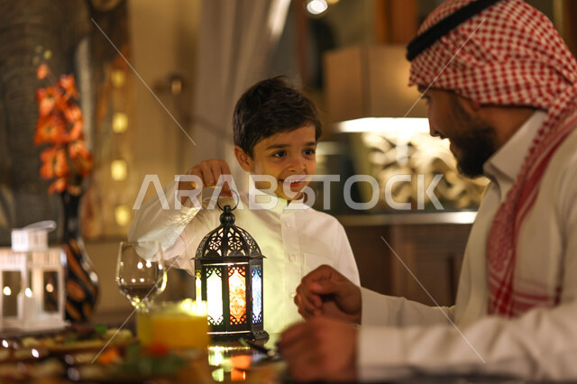 عائلة عربية خليجية سعودية على مائدة الافطار بشهر رمضان، سفرة مليئة باصناف من المأكولات اللذيذة، اب وابنه يستمتعان بتناول وجبة الافطار، ايماءات وجه سعدية، اجواء رمضانية، فانوس رمضان، شهر رمضان الكريم