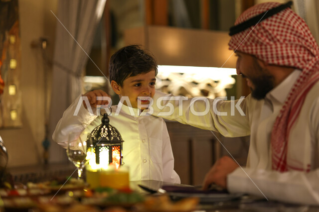 عائلة عربية خليجية سعودية على مائدة الافطار بشهر رمضان، سفرة مليئة باصناف من المأكولات اللذيذة، اب وابنه يستمتعان بتناول وجبة الافطار، ايماءات وجه سعدية، اجواء رمضانية، فانوس رمضان، شهر رمضان الكريم