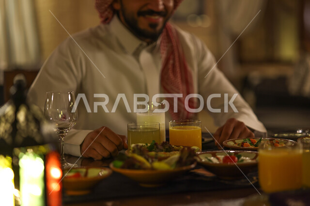 صورة مقربة لرجل عربي خليجي سعودي على مائدة الافطار بشهر رمضان، سفرة مليئة باصناف من المأكولات اللذيذة، تناول وجبة الافطار، ايماءات وجه سعدية، اجواء رمضانية، فانوس رمضان، شهر رمضان الكريم