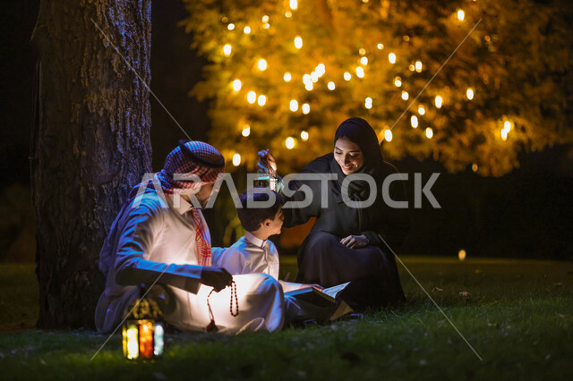 رجل عربي خليجي سعودي يعلم ابنه قراءة وتلاوة القرآن الكريم، تحفيظ القرآن للابناء، تجمع العائلة في حديقة المنزل، شهر رمضان المبارك، فانوس رمضان، إضاءة وزينة شهر رمضان، أجواء رمضانية، مناسبات دينية