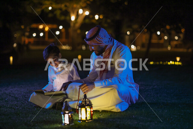 رجل عربي خليجي سعودي يعلم ابنه قراءة وتلاوة القرآن الكريم، تحفيظ القرآن للابناء، شهر رمضان المبارك، فانوس رمضان، إضاءة وزينة شهر رمضان، أجواء رمضانية، مناسبات دينية