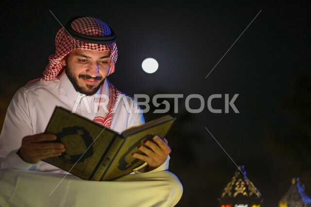 رجل عربي خليجي سعودي يمسك المصحف الشريف، فانوس رمضان، قراءة وتلاوة القرآن الكريم، حفظ القران الكريم، شهر رمضان المبارك، إضاءة وزينة شهر رمضان، أجواء رمضانية، مناسبات دينية
