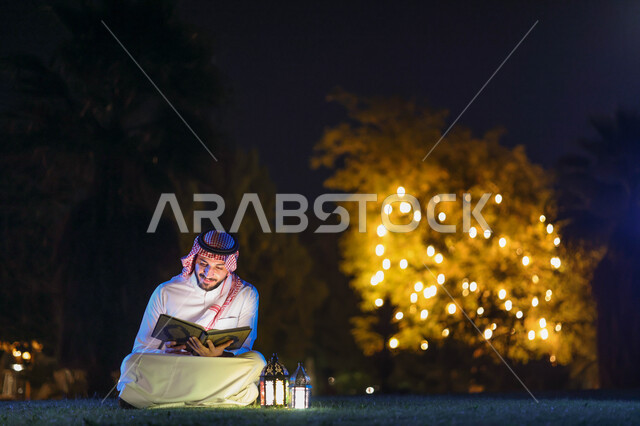 رجل عربي خليجي سعودي يمسك المصحف الشريف، فانوس رمضان، قراءة وتلاوة القرآن الكريم، حفظ القران الكريم، شهر رمضان المبارك، إضاءة وزينة شهر رمضان، أجواء رمضانية، مناسبات دينية
