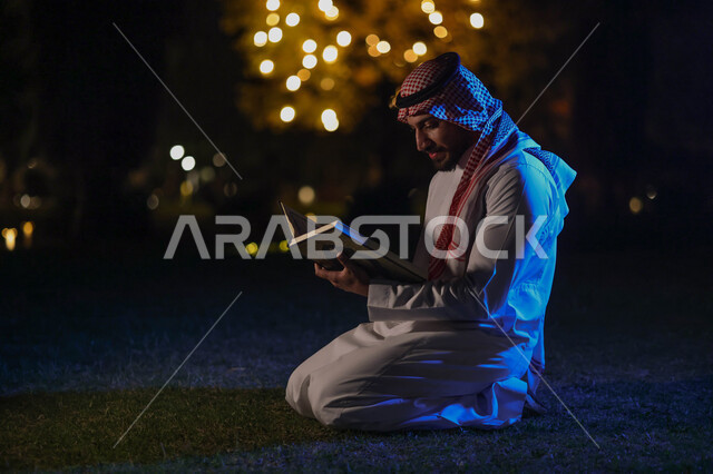 رجل عربي خليجي سعودي يمسك المصحف الشريف، قراءة وتلاوة القرآن الكريم، حفظ القران الكريم، شهر رمضان المبارك، إضاءة وزينة شهر رمضان، أجواء رمضانية، مناسبات دينية