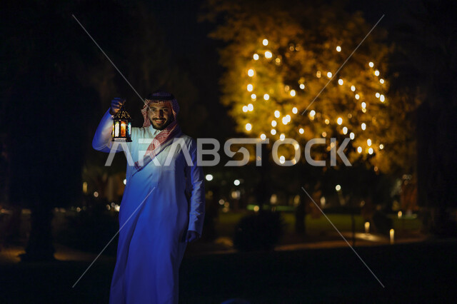 رجل عربي خليجي سعودي يمسك فانوس رمضان ويتجول في حديقة المنزل، فانوس رمضان، شهر رمضان المبارك، إضاءة وزينة شهر رمضان، أجواء رمضانية، مناسبات دينية