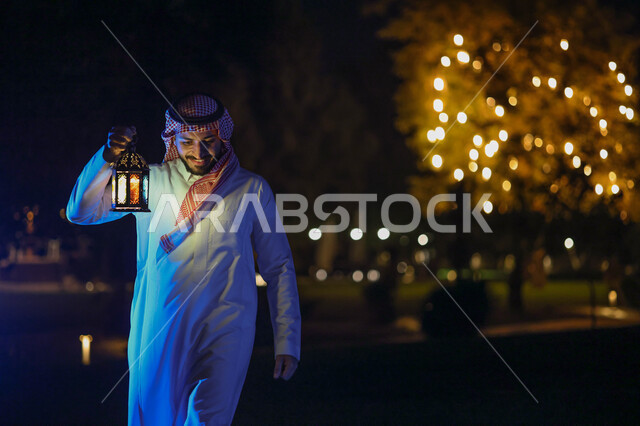 رجل عربي خليجي سعودي يمسك فانوس رمضان ويتجول في حديقة المنزل، فانوس رمضان، شهر رمضان المبارك، إضاءة وزينة شهر رمضان، أجواء رمضانية، مناسبات دينية