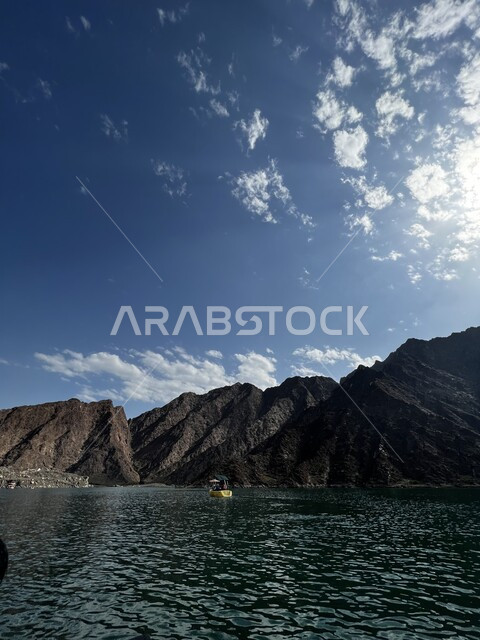 قارب في وسط بحيرة مدينة حتا بدولة الامارات العربية المتحدة، سماء زرقاء فوق جبال صخرية على بحيرة حتا، أماكن سياحية في دولة الامارات.