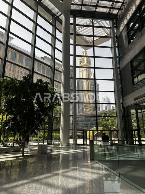 لقطة داخلية من أحد المباني الزجاجية تظهر فيها البنايات الخارجية، زراعة النباتات والأشجار الداخلية، بنايات زجاجية متطورة.