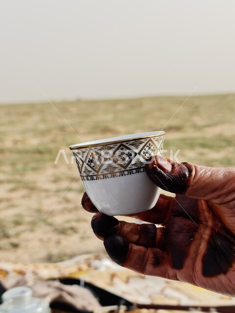 صوره مقربه ليد إمرأه مسنه تحمل بيدها فنجان القهوه العربي, القهوه السعوديه, الإستمتاع بشرب القهوه في الهواء الطلق, كشته