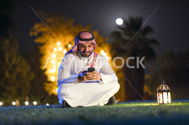 رجل عربي خليجي سعودي يستخدم الهاتف المحمول، التواصل الاجتماعي، تصفح المواقع الالكترونية،، فانوس رمضان، شهر رمضان المبارك، إضاءة وزينة شهر رمضان، أجواء رمضانية، مناسبات دينية
