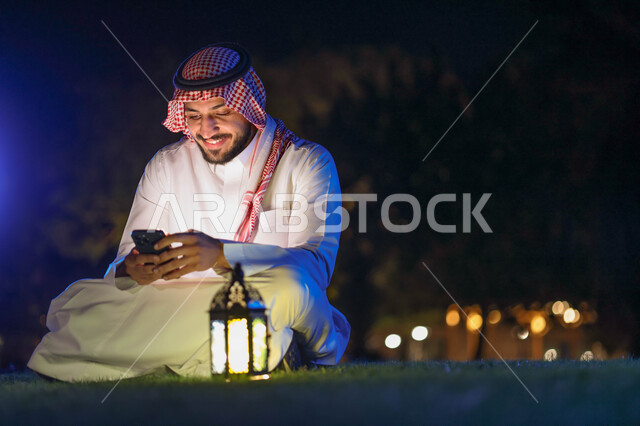 رجل عربي خليجي سعودي يستخدم الهاتف المحمول، التواصل الاجتماعي، تصفح المواقع الالكترونية،، فانوس رمضان، شهر رمضان المبارك، إضاءة وزينة شهر رمضان، أجواء رمضانية، مناسبات دينية