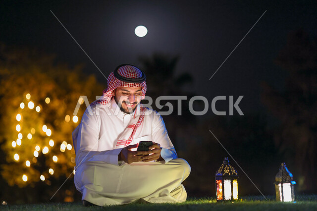 رجل عربي خليجي سعودي يستخدم الهاتف المحمول، التواصل الاجتماعي، تصفح المواقع الالكترونية،، فانوس رمضان، شهر رمضان المبارك، إضاءة وزينة شهر رمضان، أجواء رمضانية، مناسبات دينية