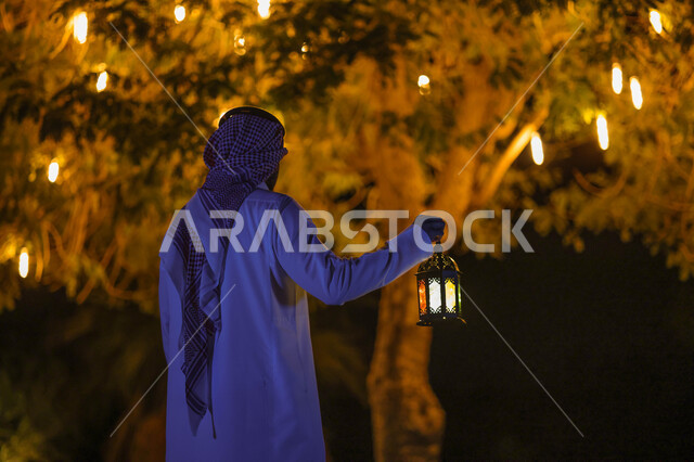 صورة من الخلف لرجل عربي خليجي سعودي يمسك فانوس رمضان، فانوس رمضان، شهر رمضان المبارك، إضاءة وزينة شهر رمضان، أجواء رمضانية، مناسبات دينية