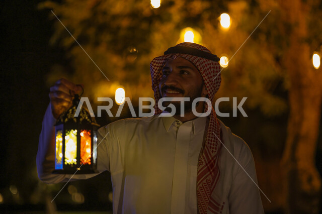 A Saudi Gulf Arab man holding a Ramadan lantern, Ramadan lantern, the blessed month of Ramadan, lighting and decorations for the month of Ramadan, Ramadan atmosphere, religious occasions