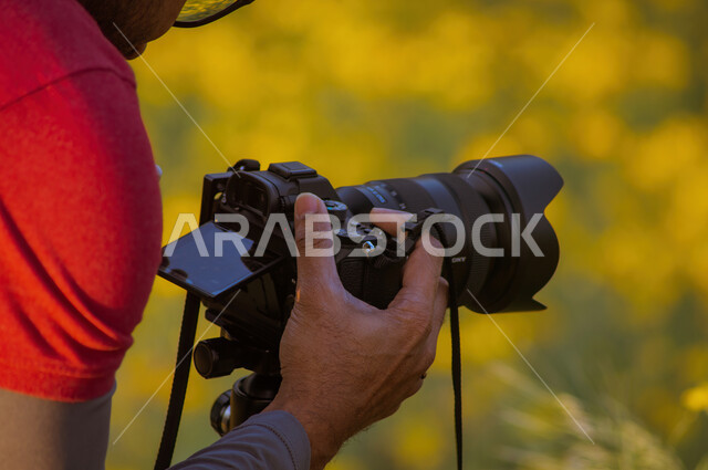 رجل يحمل بيده كاميرا تصوير عالية الدقة  ليلتقط صور احترافية، فن التصوير الفوتوغرافي ، موهبة واحتراف، التقاط صور تذكارية 