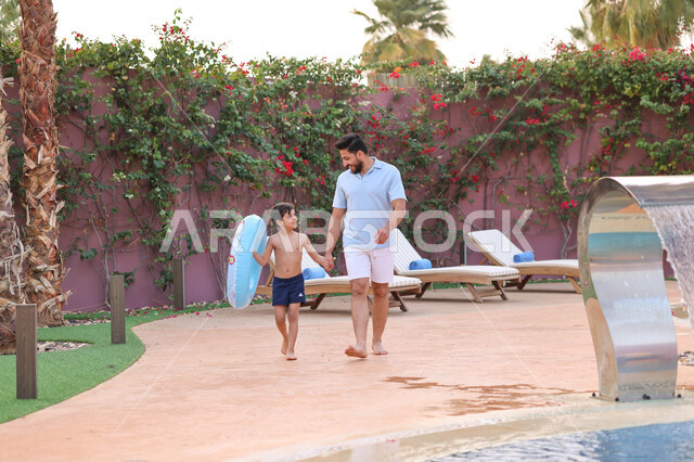 رجل عربي خليجي سعودي يقضي اوقات ممتعة مع ابنه، المشي على حدود البركة المائية، الاستعداد للسباحة في المسبح، اجواء صيفية ممتعة، رحلة سياحية ترفيهية، استخدام عوامة السباحة، عطلة صيفية سعيدة