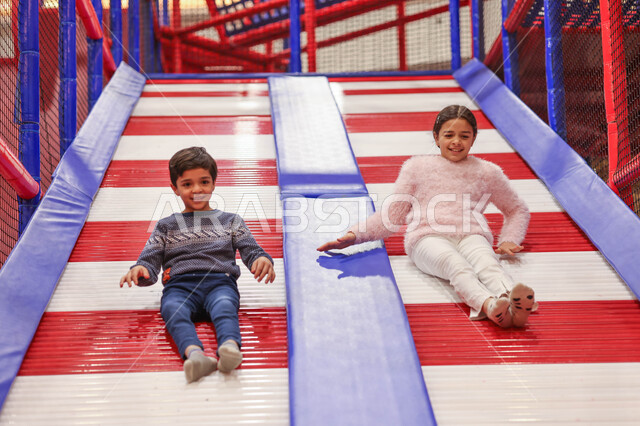 طفلان عربيان خليجيان سعوديان يستمتعان باللعب على لعبة التزحلق، التسلية والترفيه، الانشطة الترفيهية، عطلة صيفية سعيدة، قضاء اوقات ممتعة