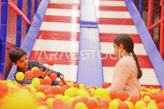 طفلان عربيان خليجيان سعوديان يستمتعان باللعب على لعبة التزحلق، التسلية والترفيه، الانشطة الترفيهية، عطلة صيفية سعيدة، قضاء اوقات ممتعة