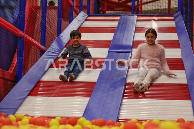 Two Saudi Arabian Gulf children enjoying playing on a skating game, entertaining and entertaining, recreational activities, happy summer vacation, spending fun times