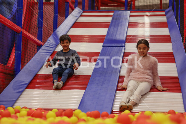 طفلان عربيان خليجيان سعوديان يستمتعان باللعب على لعبة التزحلق، التسلية والترفيه، الانشطة الترفيهية، عطلة صيفية سعيدة، قضاء اوقات ممتعة