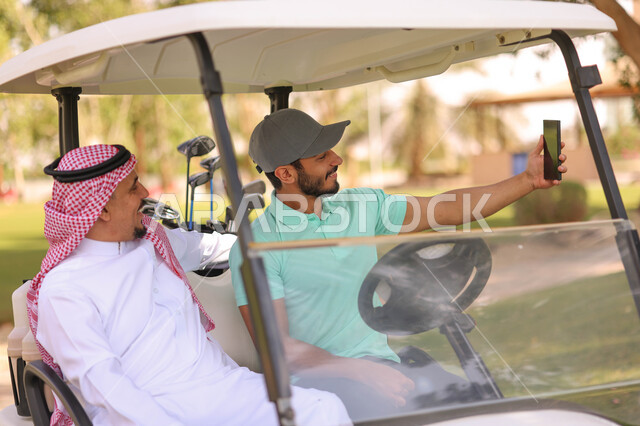 رجلان عربيان خليجيان سعوديان داخل سيارة كهربائية مختصة بنقل الركاب، إلتقاط صور سيلفي تذكاريه بإستخدام الهاتف المحمول، أنشطة رياضية بالسعودية، لعبة الجولف، رياضات الألعاب الأولمبية الصيفية، أنشطة ترفيهية