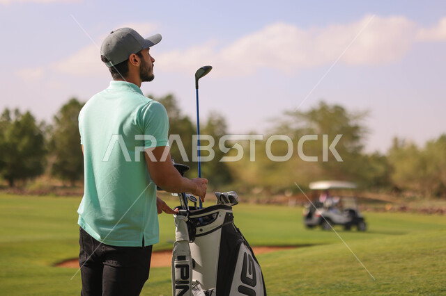 رجل عربي خليجي سعودي يحمل حقيبة الجولف، ممارسة لعبة الغولف على مساحات واسعة خضراء، أنشطة رياضية بالسعودية، لعبة الجولف، رياضات الألعاب الأولمبية الصيفية، أنشطة ترفيهية، سيارة كهربائية مختصة بنقل الركاب، ملعب الجولف