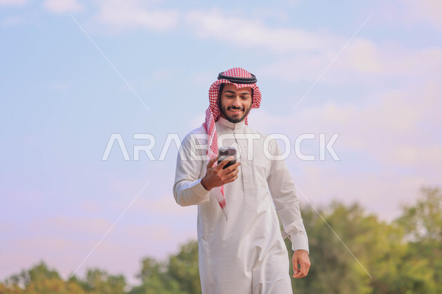 رجل عربي خليجي سعودي يتجول في احدى الحدائق العامة، استخدام الهاتف المحمول، المشي والتنزه، انشطة ترفيهية، الحدائق والمنتزهات، نزهه في الهواء الطلق