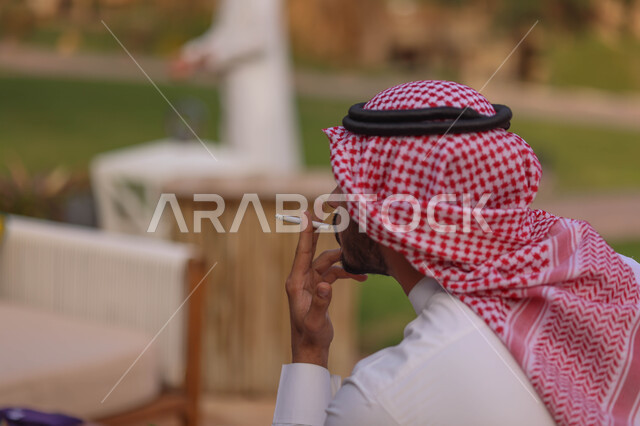 صورة مقربة لرجل عربي سعودي خليجي يقوم بتدخين السجائر، الجلوس في الهواء الطلق، الادمان على التبغ والسجائر، الطبيعة الخضراء