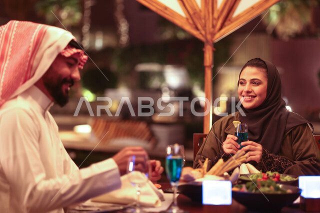 زوجان عربيان خليجيان سعوديان يستمتعان بتبادل الحديث  في احد المقاهي السعودية، تناول المشروبات الباردة، نقاشات وحوارات، قضاء أوقات ممتعة، أجواء عائلية سعيدة، مقهى سعودي