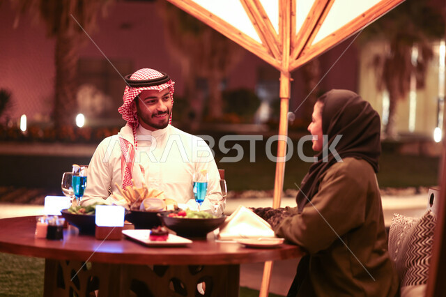 زوجان عربيان خليجيان سعوديان يستمتعان بتبادل الحديث  في احد المقاهي السعودية، تناول المشروبات الباردة، نقاشات وحوارات، قضاء أوقات ممتعة، أجواء عائلية سعيدة، مقهى سعودي