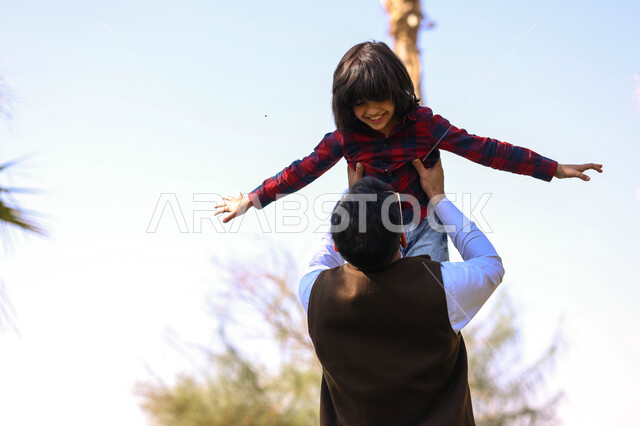 رجل عربي خليجي سعودي يقضي أوقات ممتعه مع ابنه، اللعب في إحدى الحدائق العامة, نزهه في الهواء الطلق،  الطبيعة الخضراء، أنشطة ترفيهية عائلية, عطله صيفيه