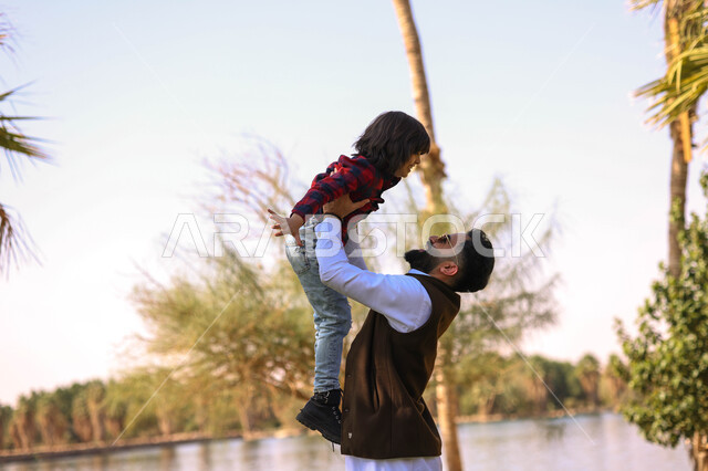 رجل عربي خليجي سعودي يقضي أوقات ممتعه مع ابنه، اللعب في إحدى الحدائق العامة, نزهه في الهواء الطلق،  الطبيعة الخضراء، أنشطة ترفيهية عائلية, عطله صيفيه