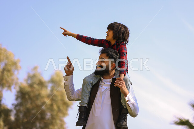 A Saudi Arabian Gulf man spends fun times with his son, playing in a public park, picnicking outdoors, green nature, family leisure activities, summer vacation