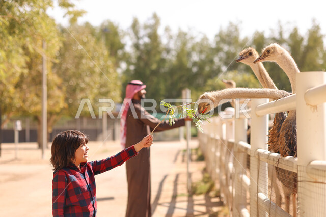 رجل عربي خليجي سعودي يقضي أوقات ممتعة مع إبنه في حديقة الحيوانات في المملكة العربية السعودية، أماكن سياحية ترفيهية بالسعودية، حيوانات برية في المحمية الطبيعية، فعالية سفاري موسم الرياض، فعاليات ترفيهية عائلية