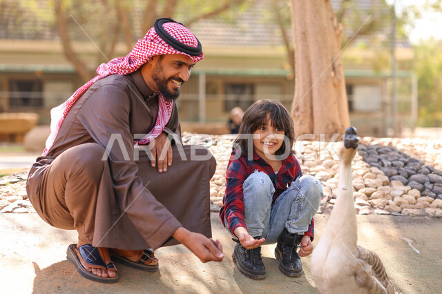 رجل عربي خليجي سعودي يقضي أوقات ممتعة مع إبنه في حديقة الحيوانات في المملكة العربية السعودية، أماكن سياحية ترفيهية بالسعودية، حيوانات برية في المحمية الطبيعية، فعالية سفاري موسم الرياض، فعاليات ترفيهية عائلية