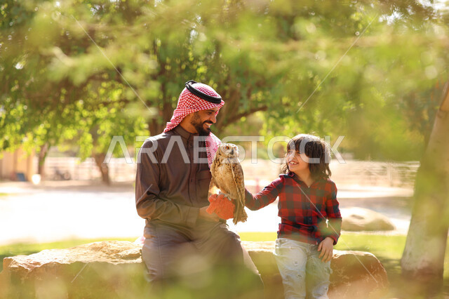 رجل عربي خليجي سعودي مع إبنه، قضاء أوقات ممتعة في حديقة الحيوانات في المملكة العربية السعودية، أماكن سياحية ترفيهية، أنشطة ترفيهية مع الطيور، تربية وتدريب الطيور الجارحة في المحمية الطبيعية، طائر البومة