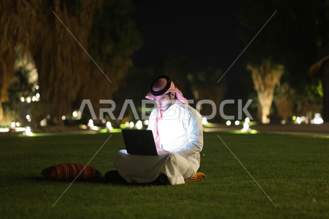 رجل عربي خليجي سعودي يستخدم الحاسوب المحمول، إنجاز مهام العمل، تصفح الإنترنت، العمل عن بعد، دردشة الكترونية، استخدام تقنيات حديثة، حدائق ومنتزهات