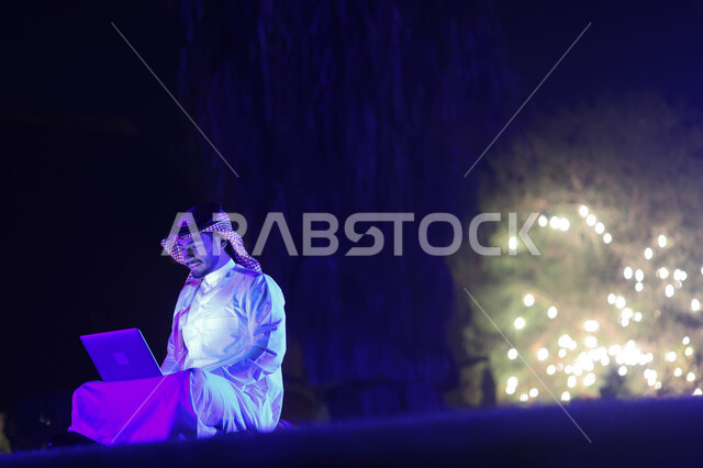 رجل عربي خليجي سعودي يستخدم الحاسوب المحمول، إنجاز مهام العمل، تصفح الإنترنت، العمل عن بعد، دردشة الكترونية، استخدام تقنيات حديثة، حدائق ومنتزهات