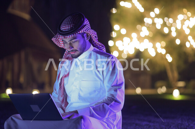 A Saudi Arabian Gulf man using a laptop, completing work tasks, surfing the Internet, working remotely, chatting electronically, using modern technologies, gardens and parks