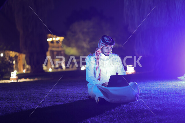 رجل عربي خليجي سعودي يستخدم الحاسوب المحمول، إنجاز مهام العمل، تصفح الإنترنت، العمل عن بعد، دردشة الكترونية، استخدام تقنيات حديثة، حدائق ومنتزهات